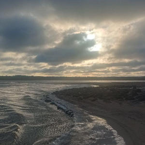 Солнце пробивается сквозь тучи над волной